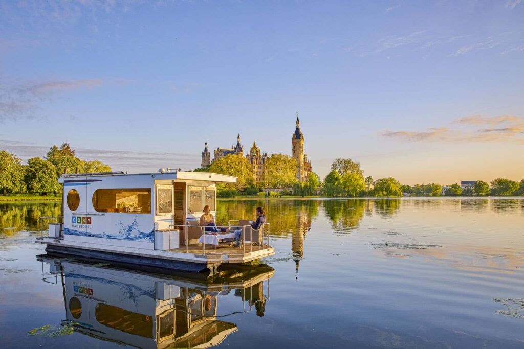 Hausboot schwimmt auf dem Schweriner See im Hintergrund ist das Schweriner Schloss zu erkennen, VINDUA Hausboote in Schwerin, Hausboot mieten und Urlaub in M-V machen