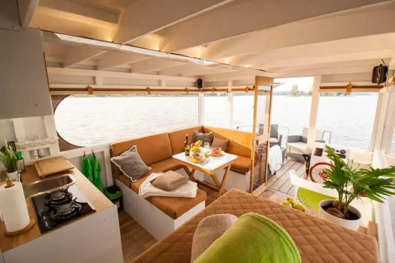 Wohnbereich eines Hausbootes mit moderner heller Einrichtung in weiß und braun mit grünen Akzenten, Küche und Couch in einem Hausboot, Über uns VINDUA